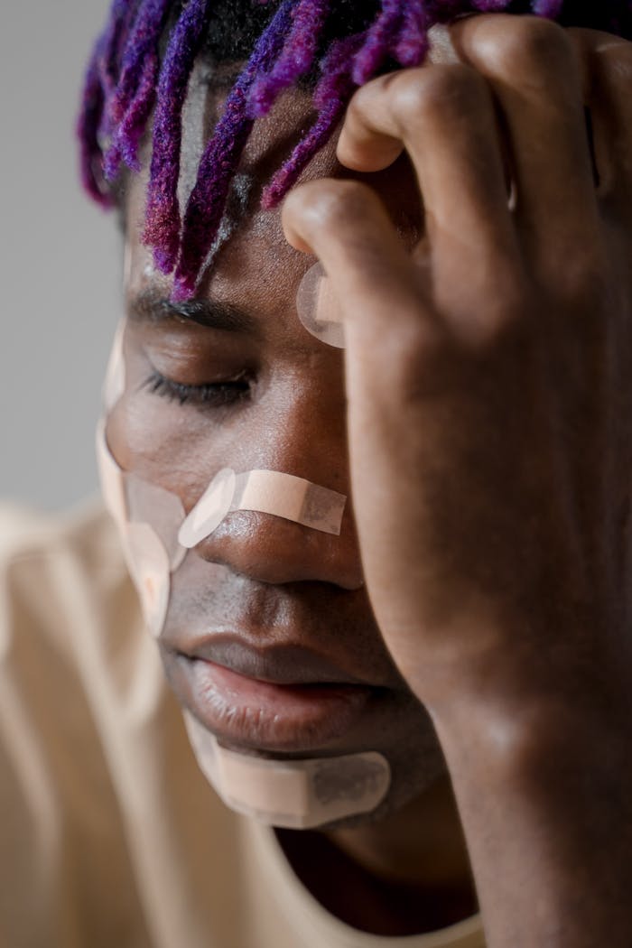 Close-up of a man with bandages on his face, expressing deep thought or sadness.